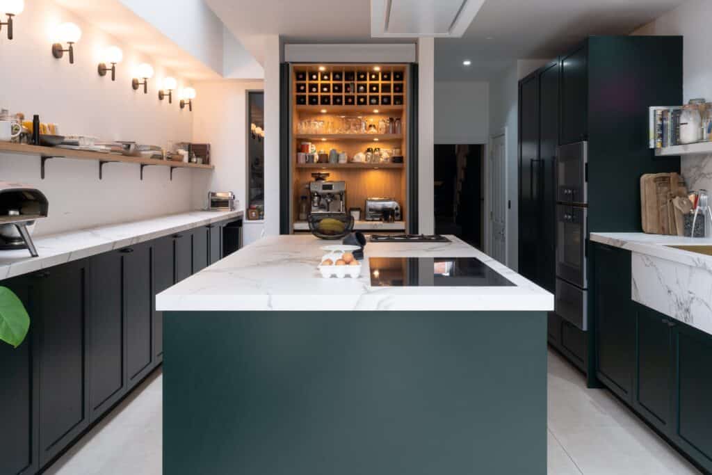 A London kitchen featuring green cabinets and marble countertops, designed by Wood Works for a bespoke experience.
