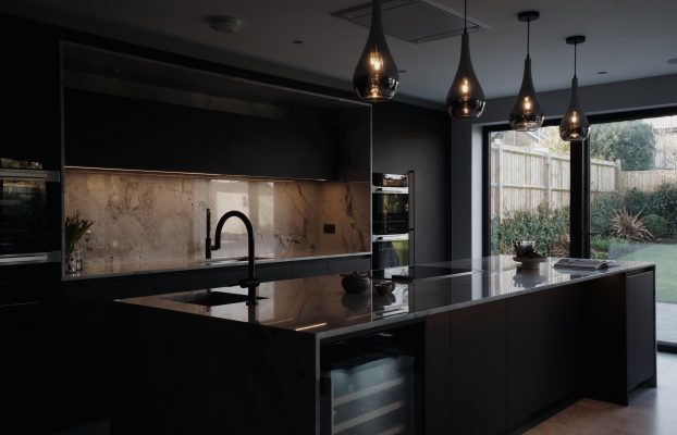 A bespoke black kitchen with a large island and a glass door.