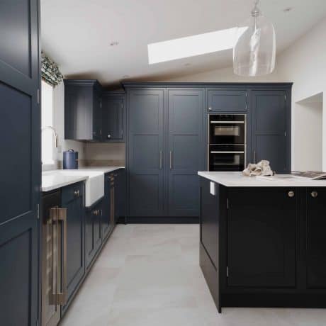 A bespoke kitchen in London featuring dark blue cabinets and white counter tops.