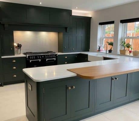 A bespoke kitchen in London with dark green cabinets and white countertops.